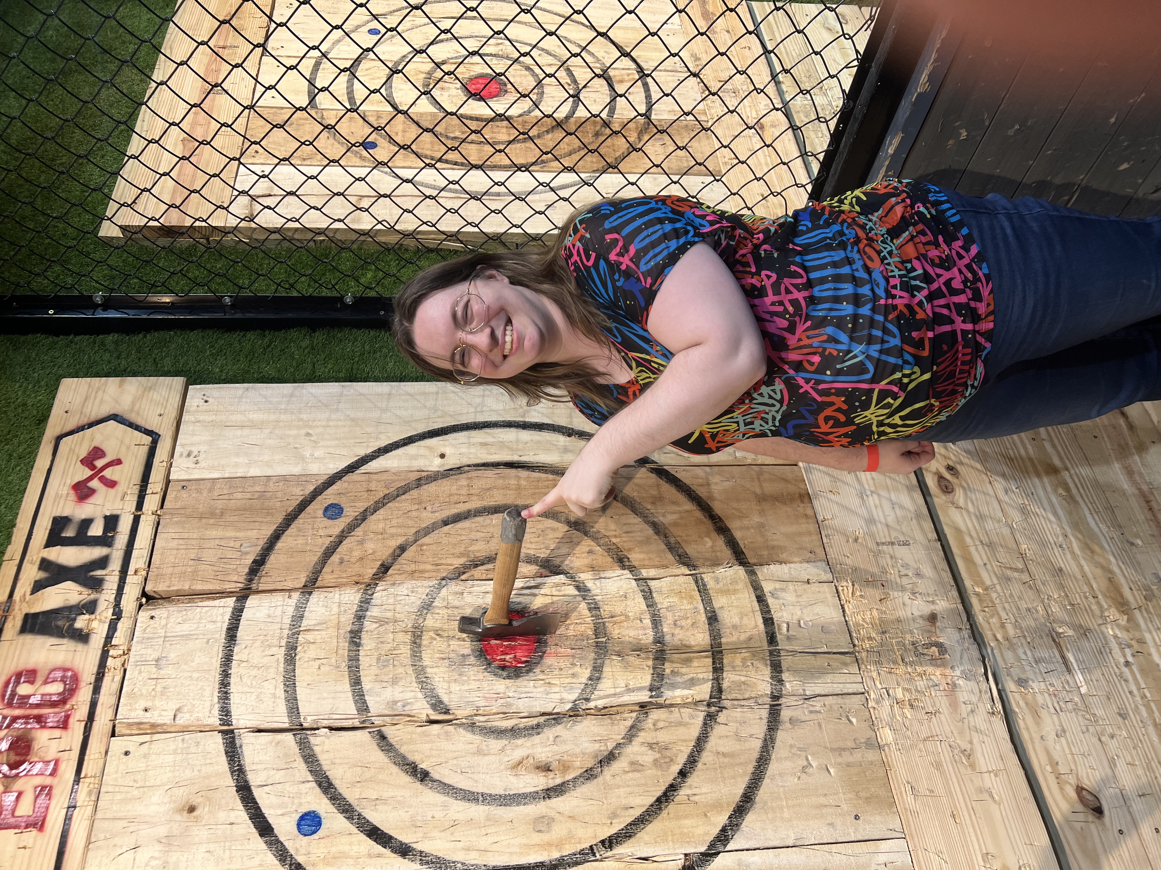 Me grinning and pointing at the handle of an axe nestled in the center of a bullseye